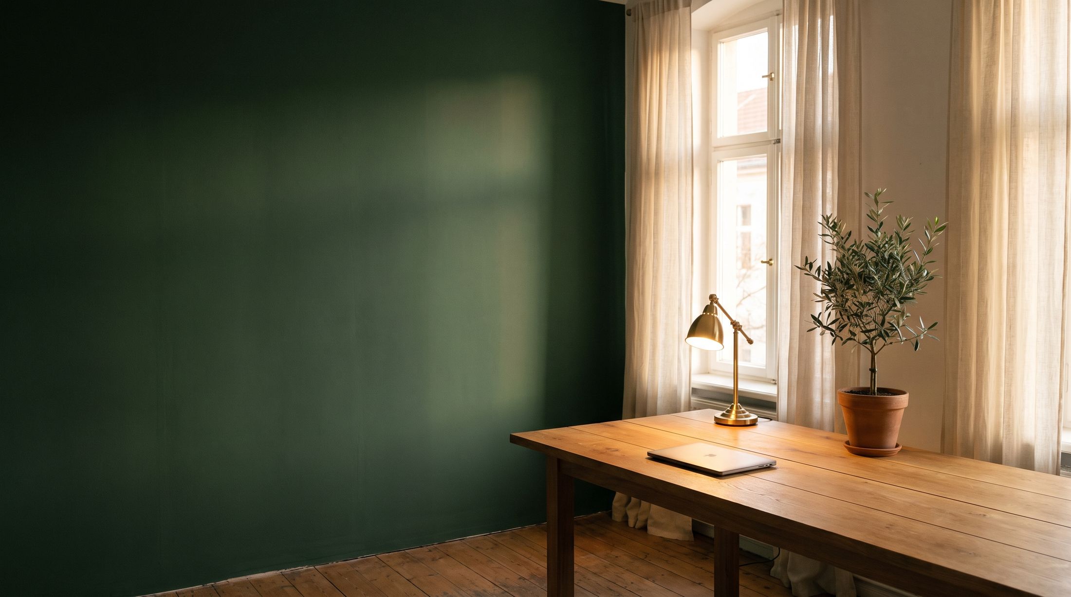 Symbolbild (KI-generiert): ruhiger Arbeitsraum mit waldgrüner Wand, Eichentisch, Messinglampe und Olivenbaum im Abendlicht